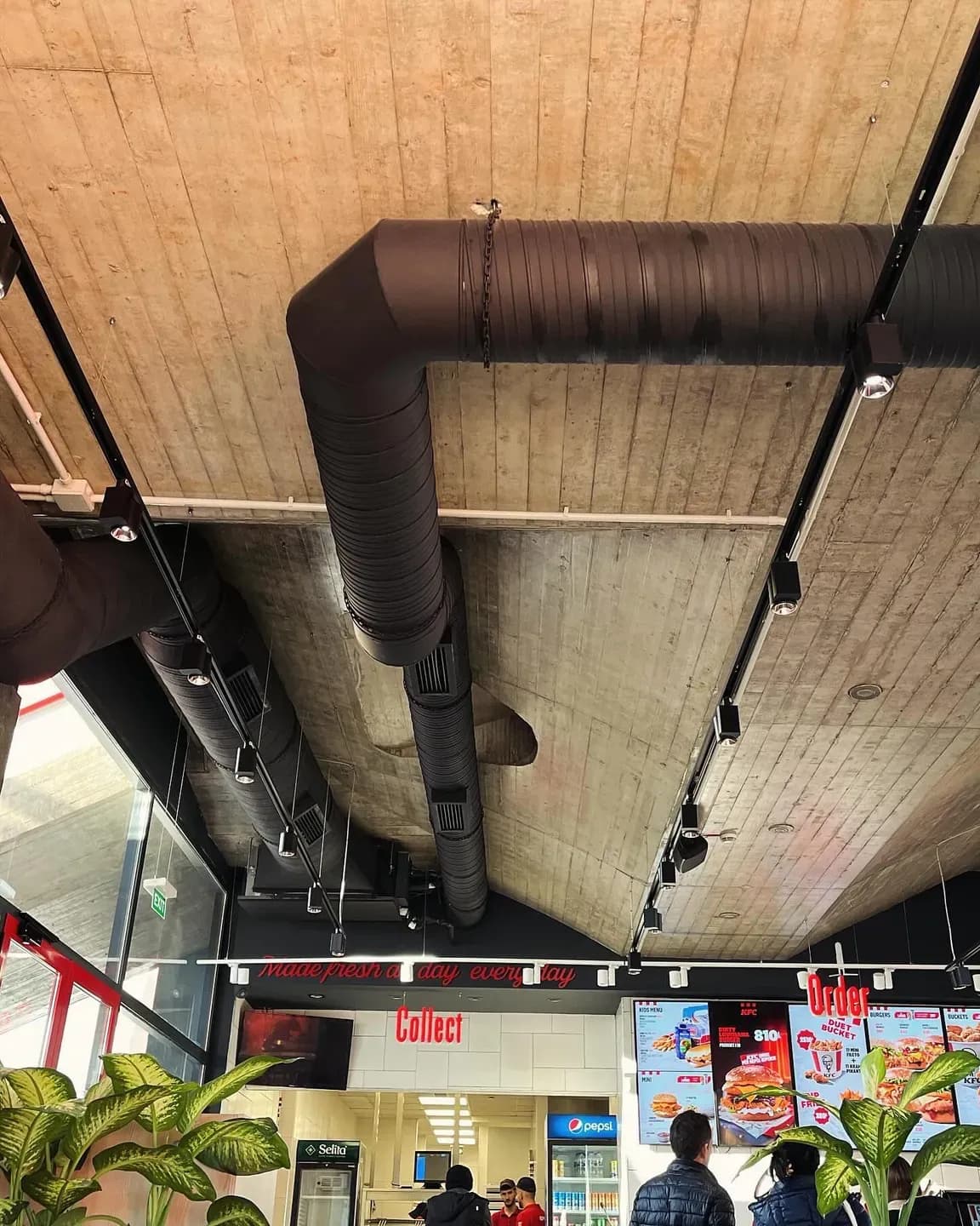 Kanale ventilimi të dukshme nën tavanin prej druri të një lokali