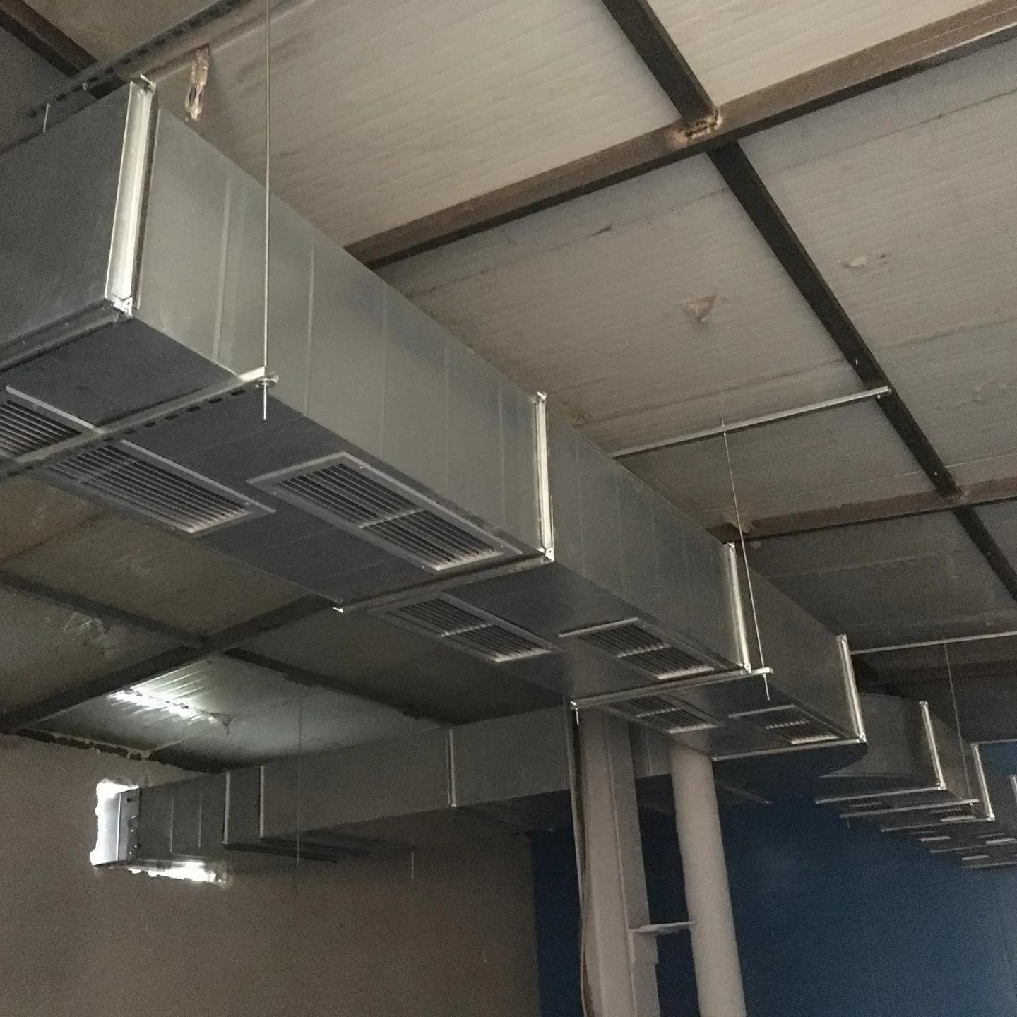 Linjë kanalesh ventilimi me grila shpërndarjeje ajri në një ambient industrial
